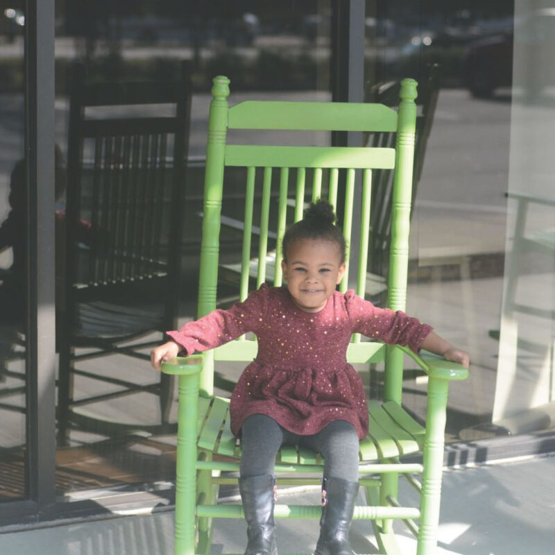 Cover of our strategic plan, shows a little girl sitting on a rocking chair on the front porch of the green chair project.